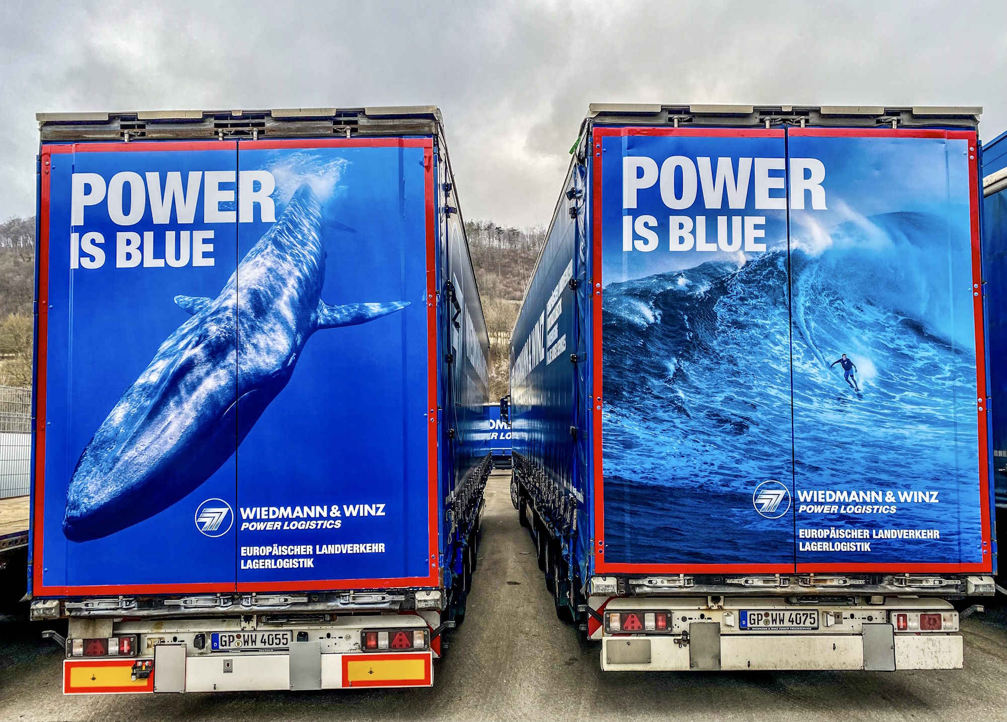 Zwei Lkw parken nebeneinander. Auf dem Heck ist ein auffälliges blaues Motiv mit einem Wal und einem Surver zu sehen.